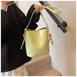 Detail of light green bucket bag showing wrinkled leather texture and pearl doll charm