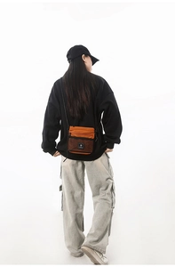 Detail of orange canvas crossbody bag with black mesh pocket shown on a model's back