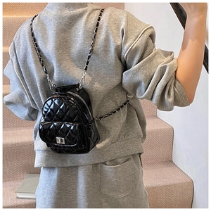 Detail of a mini black quilted leather backpack featuring silver chain straps on model