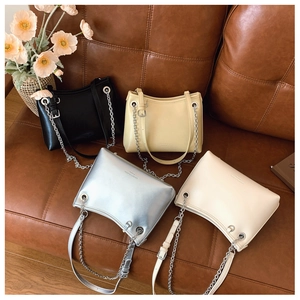 Détail de sacs seaux minimalistes avec bandoulières dorées sur un canapé en cuir