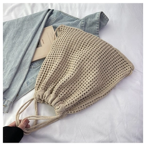 Detail of beige woven drawstring bucket bag showing hollow mesh texture and rope straps
