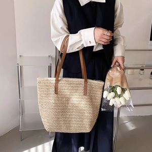 Détail du sac cabas en paille tissée avec anses en cuir marron tenu par un mannequin