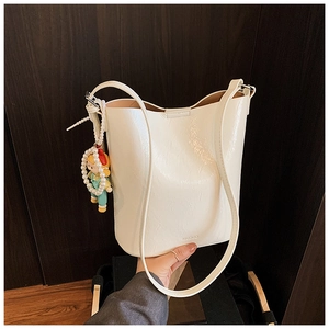 Close-up of white bucket bag featuring a pearl doll charm and embossed brand logo