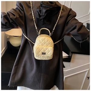 Detail of a beige quilted leather mini backpack with woven chain straps on a model back
