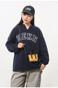 Détail d'un mini sac bandoulière jaune gingembre porté avec un sweat-shirt bleu marine foncé