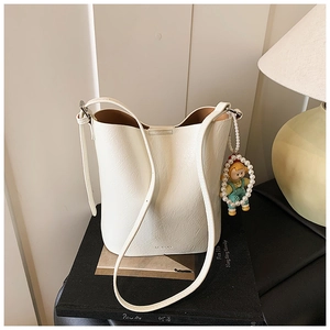 Detailed view of white textured leather bucket bag with cute pendant and brand logo