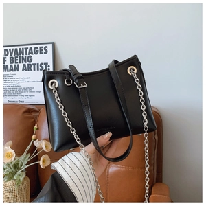 Gros plan d'un sac seau en cuir noir avec chaîne argentée et poignée porté à la main