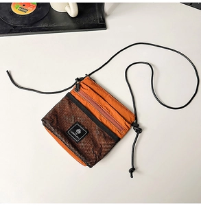 Detail of burnt orange nylon crossbody bag featuring black mesh pocket and rope strap