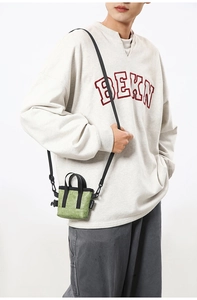 Mini sac bandoulière vert avec poignées noires porté par un mannequin en pull