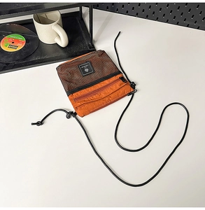 Detail of orange nylon crossbody bag with mesh pocket and dual zippers on white desk