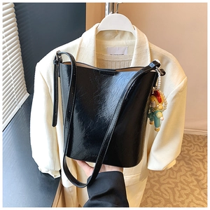 Detail of a black textured bucket bag with a cute cartoon charm on a neutral background
