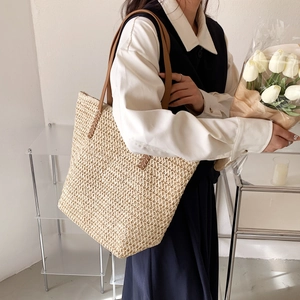 Gros plan sur la texture en paille tressée et les anses en cuir marron du sac cabas beige
