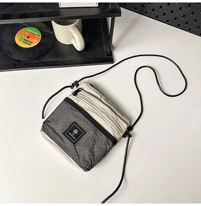 Detail of a functional cream crossbody bag with mesh pocket and logo on an aesthetic desk