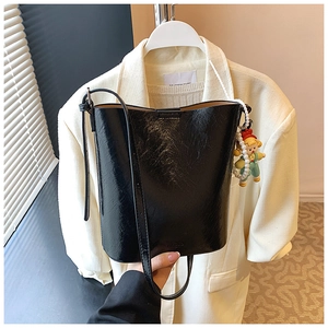Macro shot of black glossy patent leather bucket bag with pearl and doll charm