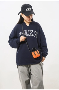 Détail d'un mini sac bandoulière orange avec anses noires sur une tenue décontractée