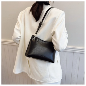 Détail du sac demi-lune noir avec chaîne argentée porté sur un blazer blanc ajusté