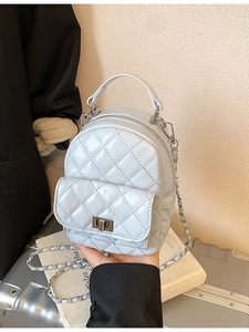 Light blue quilted mini backpack with leather chain straps on a silver suitcase