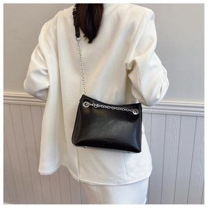 Détail d'un sac à bandoulière en cuir noir avec chaîne argentée et pieds métalliques