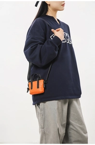 Détail d'un mini sac bandoulière orange vif avec sangle noire et étiquette de marque