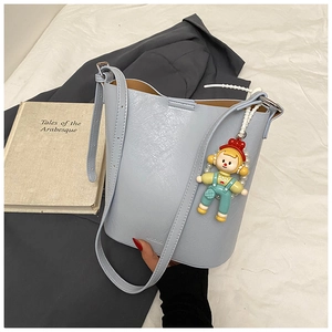 Detail of light blue leather bucket bag with cute cartoon pendant on white fabric