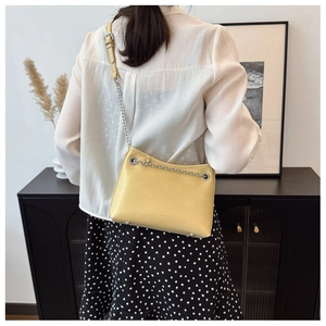 Sac seau jaune en similicuir avec bandoulière chaîne porté par un mannequin chic