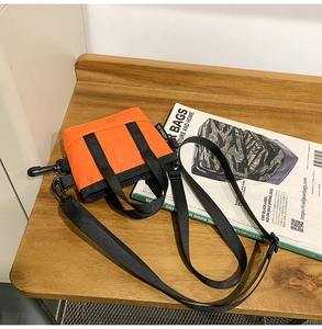 Détail d'un sac bandoulière orange en nylon avec poignées tissées sur une table en bois