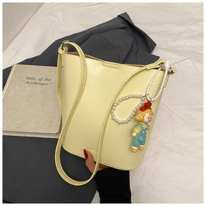 Detail of a yellow leather bucket bag with cute pearl charm on white bedding