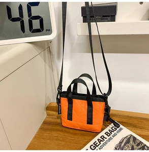 Détail d'un mini sac cabas orange avec poignées noires et étiquette de marque tissée