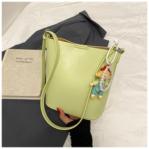 Close-up of lime green bucket bag with lychee texture, doll pendant and pearl chain