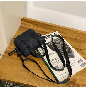 Mini sac bandoulière noir avec texture plissée et sangle réglable sur une table en bois