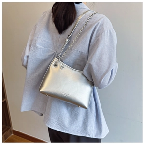 Détail du sac à bandoulière argenté montrant la texture cuir métallisé et les pieds en métal