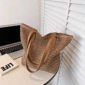 Détail du sac cabas en paille tissé avec anses en cuir marron et fermeture éclair en métal