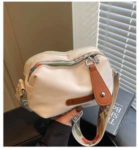Detailopname van een crème nylon crossbody tas met kleurrijke geweven band en ritsen