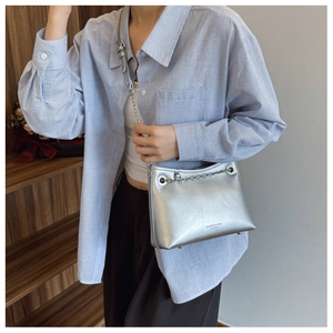 Détail du sac bandoulière argenté métallisé avec chaîne et logo sur chemise rayée