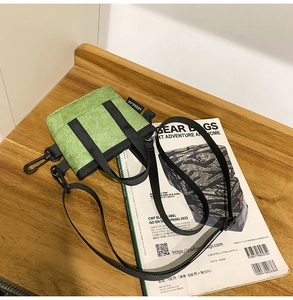 Détail du sac bandoulière vert texturé sur table en bois avec sangle nylon et logo