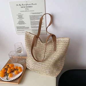 Détail d'un sac cabas en paille avec bandoulières en cuir marron et fermeture éclair