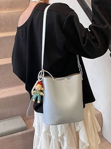Silver metallic bucket bag with adjustable strap and doll charm shown on model