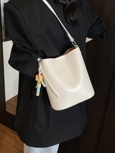Chic off-white bucket bag with pearl chain and cartoon charm shown on a shoulder
