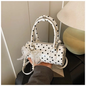 Close-up of white polka dot cylinder handbag with pearl charm and mesh bow detail
