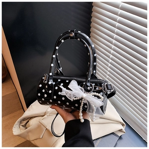 Detail of black polka dot barrel bag with white lace bow and pearl pendant charm