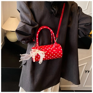 Macro detail of red polka dot cylinder bag with glossy finish and pearl bow charm