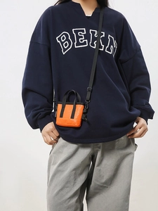 Petit sac bandoulière orange pour téléphone porté sur un sweat à capuche bleu marine foncé