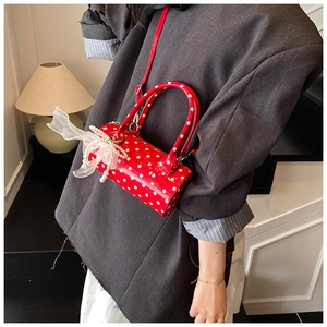 Detailed view of red polka dot cylinder bag with pearl and lace bow charm