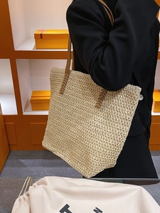 Sac fourre-tout en paille avec anses en cuir marron porté à l'épaule dans une boutique