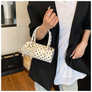 Close-up of white polka dot cylinder bag featuring lace bow charm and pearl detail