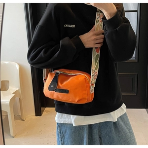 Detail van oranje oxford crossbodytas met een brede schouderband met bloemenborduurwerk