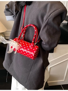 Red polka dot cylinder crossbody bag with pearl chain and bow detail on a model