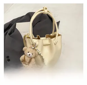 Detail of cream pleated bucket bag with lychee leather texture and cute bear charm