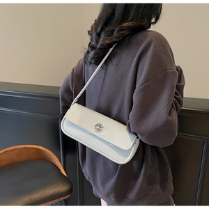 Nahaufnahme der hellgrauen Lackleder-Schultertasche mit Metallverschluss am Modell