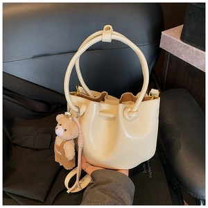 Close-up of a beige pleated bucket bag with metal ring handle and a cute teddy bear charm